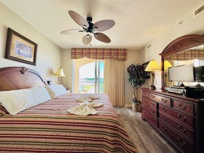 Une chambre d’hôtel équipée d’un lit, d’un ventilateur de plafond, d’une commode, d’une télévision et d’une fenêtre avec des rideaux.