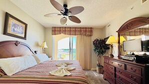 Habitación de hotel con cama, ventilador de techo, cómoda, televisor y ventana con cortinas.