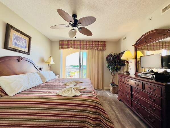 A hotel room with a bed, a ceiling fan, a dresser, a television, and a window with curtains.