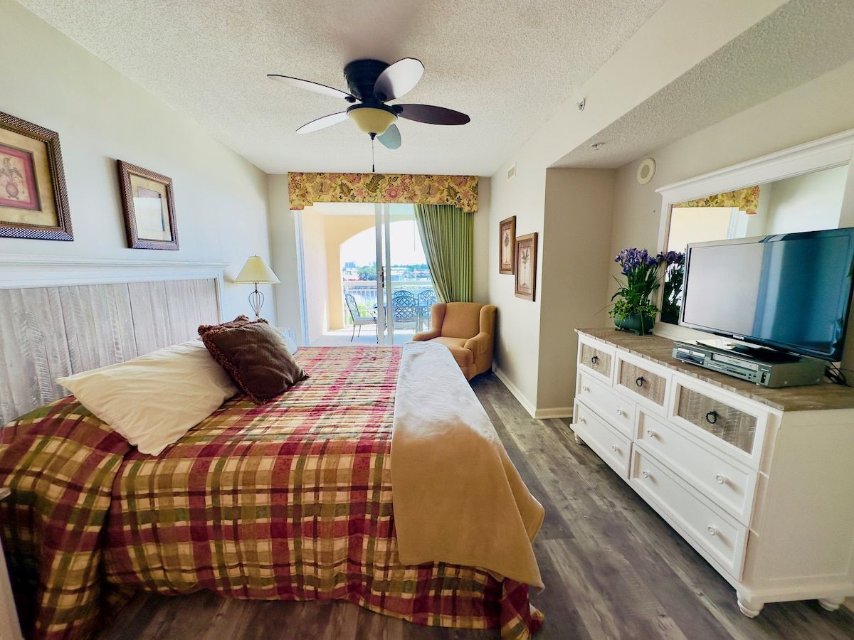 Ein Schlafzimmer mit einem Bett, einem Schminktisch, einem Fernseher und einem Deckenventilator.