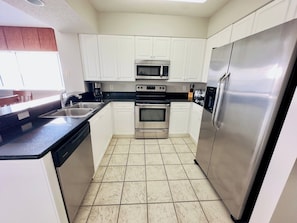 Una cocina compacta con armarios blancos, un refrigerador de acero inoxidable, un microondas, un horno doble y un lavavajillas.