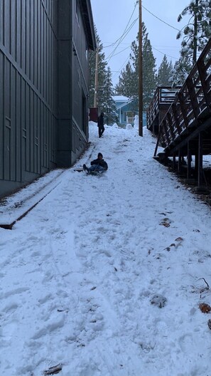 Pathway leads to a building with a metal exterior, flanked by snow-laden trees and a wooden structure.