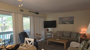 A living room with a sofa, a television, a coffee table, and a dining table with placemats. - Enjoy the Sun & White Sand in Destin!!! (Destin)