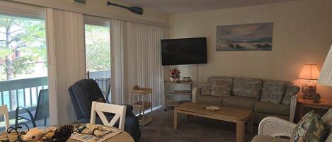 A living room with a sofa, a television, a coffee table, and a dining table with placemats.