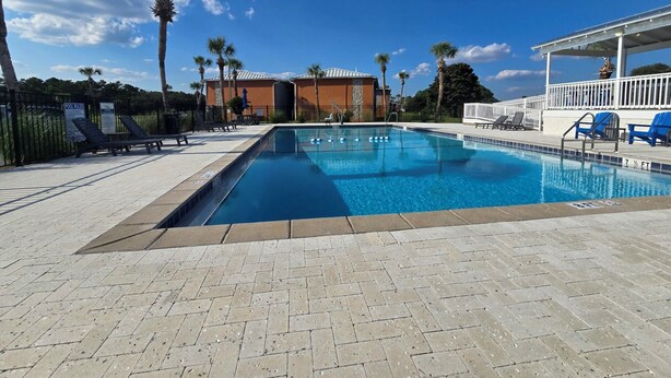 A swimming pool with lounge chairs and a covered area, surrounded by palm trees and a building. - Enjoy the Sun & White Sand in Destin!!! (Destin)