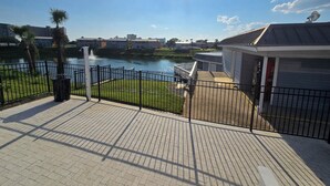 A waterfront view with a paved walkway, a fence, and a building with a roof. - Enjoy the Sun & White Sand in Destin!!! (Destin)