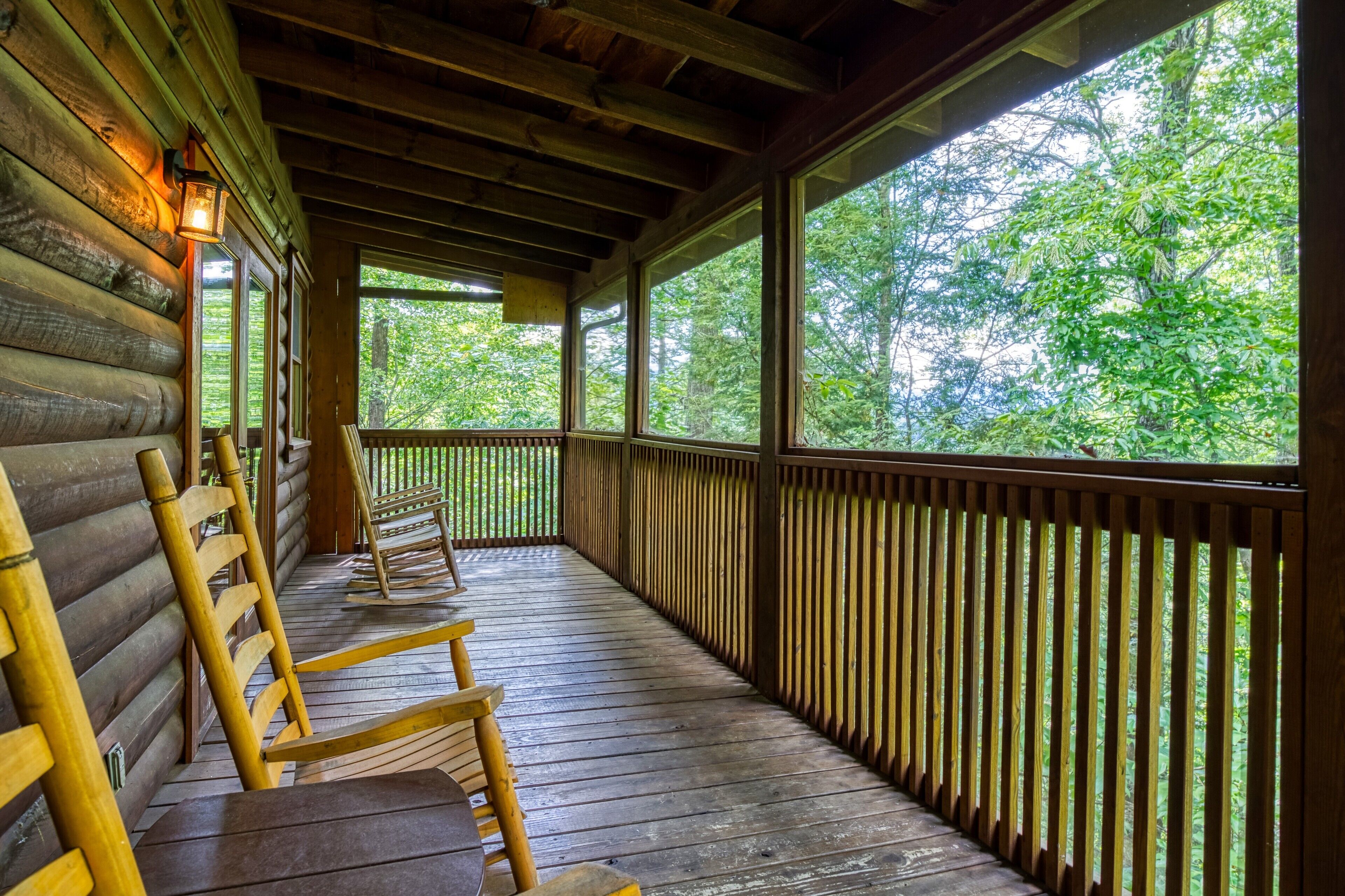 A wooden porch with a railing, wooden benches, and a view of a forest through large windows.