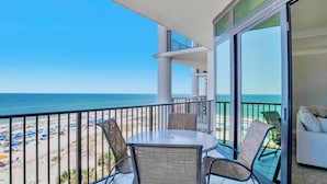 A balcony with a table and chairs, overlooking a beach with umbrellas and people.