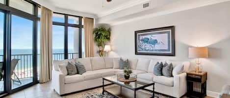 A spacious living room with a large sectional sofa, a coffee table, and a view of the ocean through large windows.