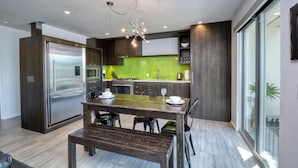 A modern kitchen with a stainless steel refrigerator, a dining table with four chairs, and a green backsplash. - Wave (2 bedroom / 2 bath) (Carlsbad)