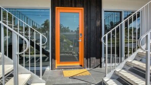 A modern building entrance with a glass door, metal railings, and a wooden door frame. - Wave (2 bedroom / 2 bath) (Carlsbad)