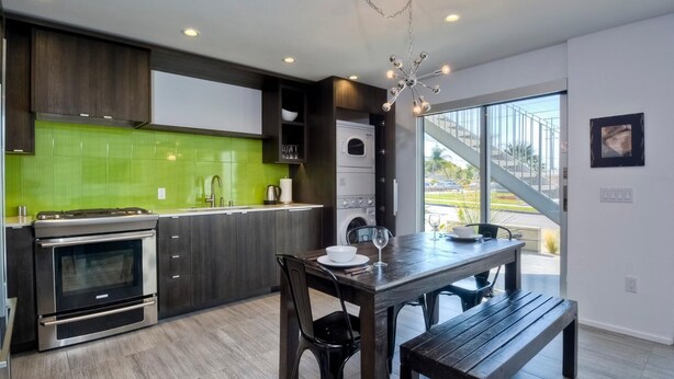 A modern kitchen with a green backsplash, stainless steel appliances, and a dining area with a bench. - Wave (2 bedroom / 2 bath) (Carlsbad)