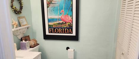 Un baño con inodoro, lavabo con tocador, un cuadro enmarcado de una playa de Florida y un perchero.