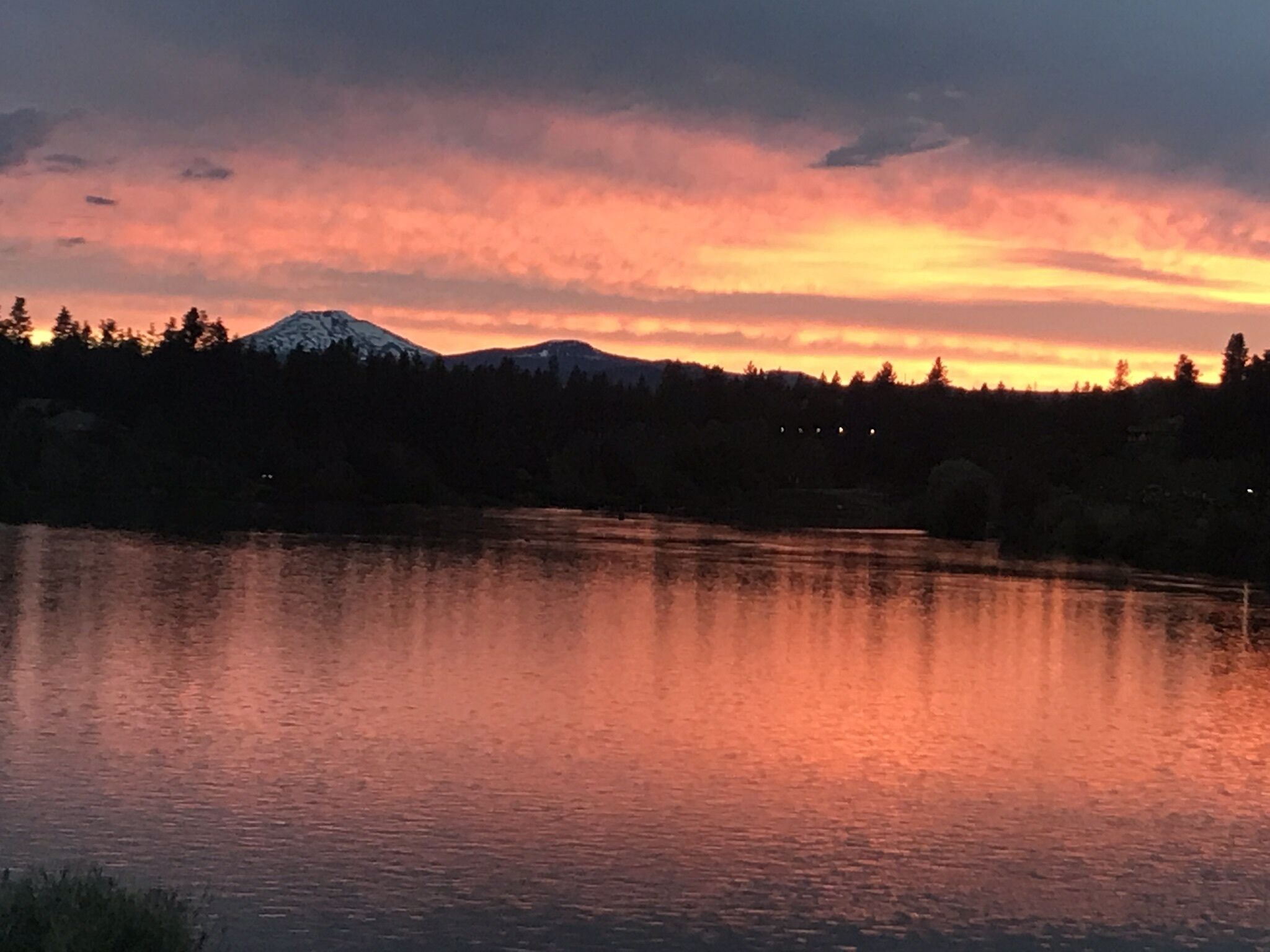A calm lake reflecting a sunset with mountains in the background.