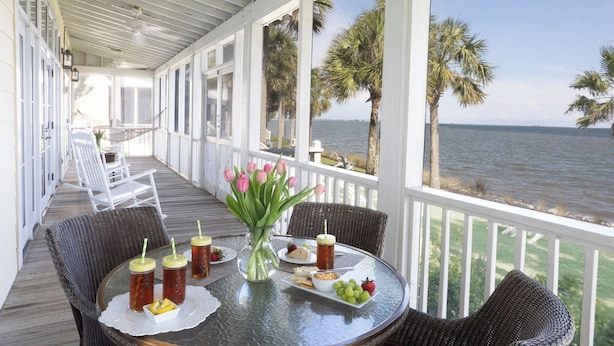 Un espace extérieur abrité avec des chaises en osier, une table en verre sur laquelle sont disposés des plats et des boissons, et une vue sur l’océan.