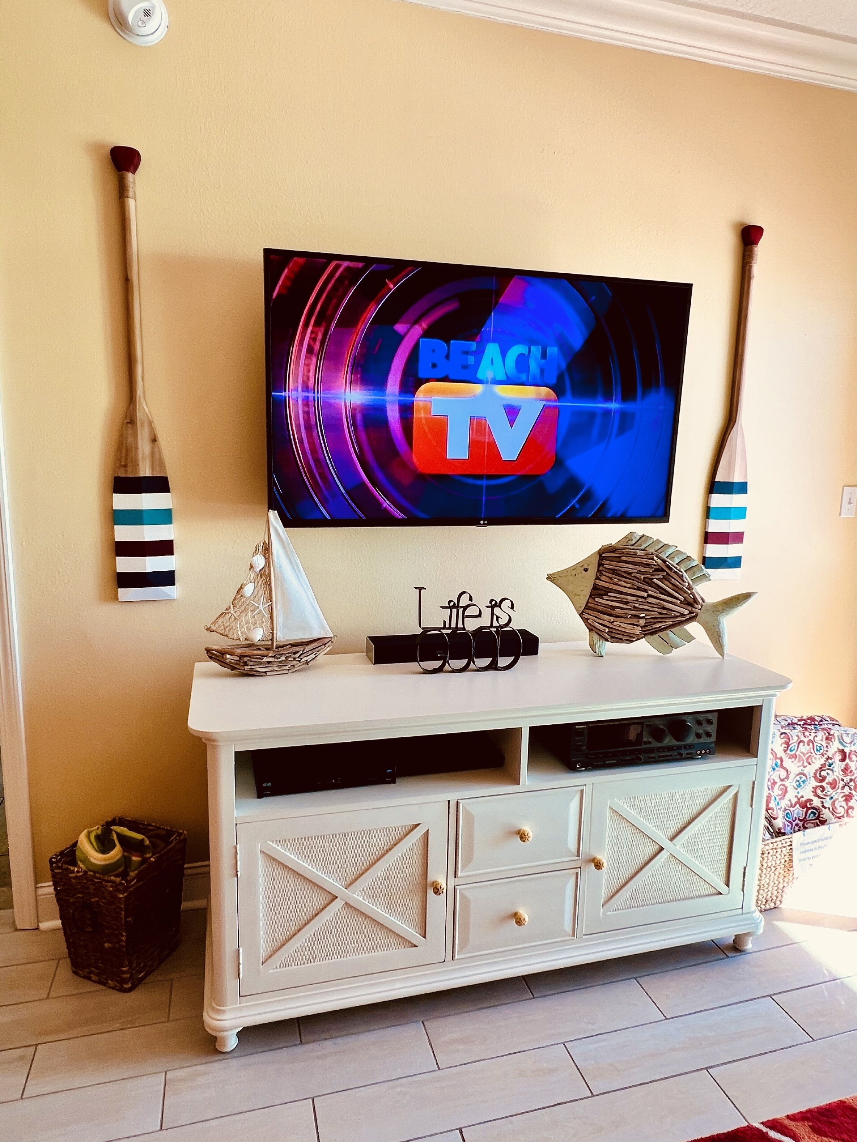 A living room with a TV mounted on the wall, a white entertainment unit with drawers, and decorative items like a star and a basket.