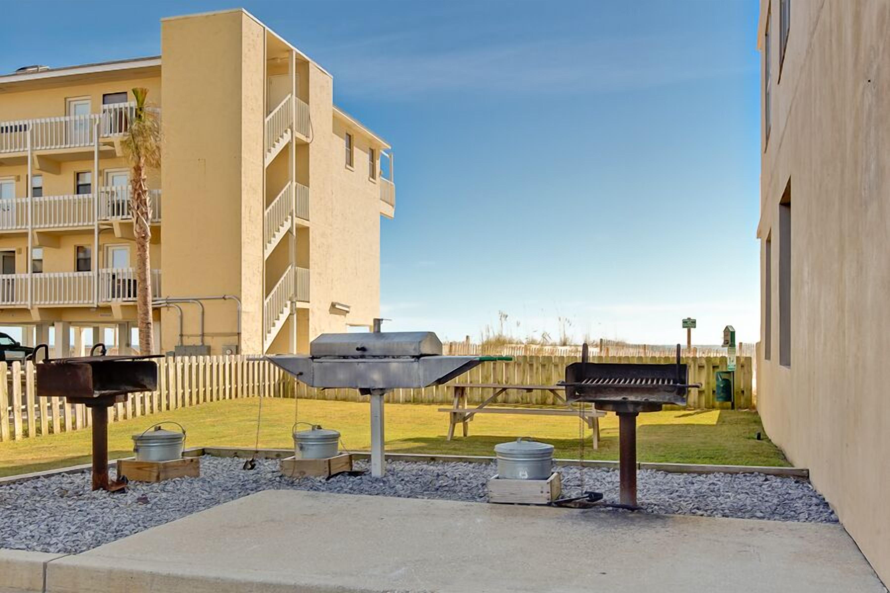 An outdoor barbecue area with grills and pots, surrounded by a fence and a building in the background.