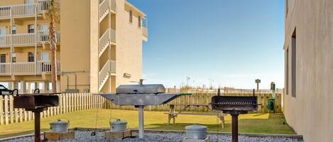 An outdoor barbecue area with grills and pots, surrounded by a fence and a building in the background.