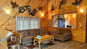 L’intérieur d’un chalet confortable, avec des murs en rondins de bois, une table à manger en bois, deux canapés, une table basse et un miroir.