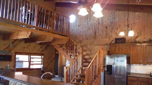 L’intérieur d’un chalet rustique est agrémenté d’un escalier en bois, d’un coin cuisine avec un réfrigérateur en acier inoxydable et d’un comptoir-bar.