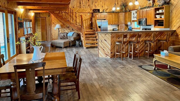 L’intérieur d’un chalet rustique comprend un coin repas en bois, un canapé, une cuisine avec des meubles en bois et un escalier.