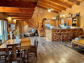 Een rustiek houten interieur met een eethoek, een bank, een keuken met houten kastjes en een trap.