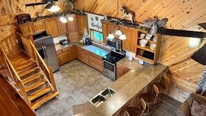 Une cuisine avec des meubles en bois, une cuisinière, un four à micro-ondes et un évier. On y trouve également un coin bar avec des tabourets et un escalier menant à un autre niveau.