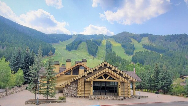 A log cabin hotel with a stone foundation, large windows, and a view of a mountain range. - Cottonwood Studio  in Sun Valley (Sun Valley)