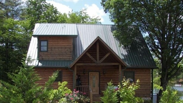 A log cabin with a gabled roof, a front porch, and a small garden with various plants and flowers.