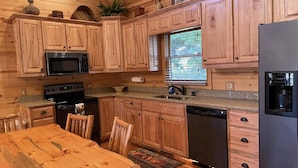 A kitchen with wooden cabinets, granite countertops, a stainless steel refrigerator, and a window with blinds.