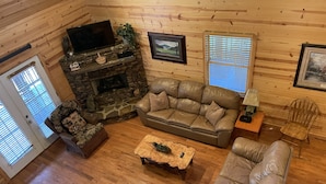 A cozy cabin interior with a stone fireplace, leather sofas, and a television.