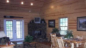 A cozy cabin interior with a stone fireplace, wooden dining table, and chairs.