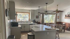 A modern kitchen with a central island, a dining area with wooden chairs, and a ceiling fan. - A Beautiful And Serene Lake View House (Julian)