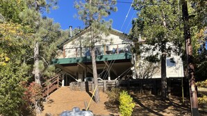 A two-story house with a covered porch, surrounded by trees and a large metal sculpture. - A Beautiful And Serene Lake View House (Julian)