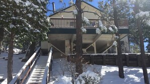 A wooden cabin with a balcony, surrounded by snow-covered trees and a staircase leading up to it. - A Beautiful And Serene Lake View House (Julian)