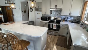 A modern kitchen with a central island, stainless steel appliances, and a stone backsplash. - A Beautiful And Serene Lake View House (Julian)