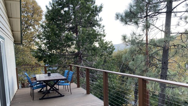 A wooden deck with a table and chairs, surrounded by trees and a view of a road. - A Beautiful And Serene Lake View House (Julian)