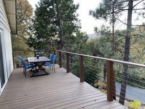 Eine Holzterrasse mit Tisch und Stühlen, umgeben von Bäumen und Blick auf eine Straße.