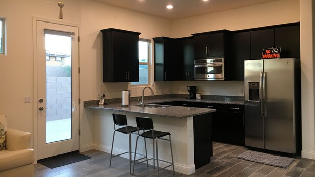 A modern kitchen with dark cabinets, stainless steel appliances, and a bar area with two stools. - Private One Bedroom Furnished Unit in Rancho Vistoso Eagles Summit Subdivision (Oro Valley)