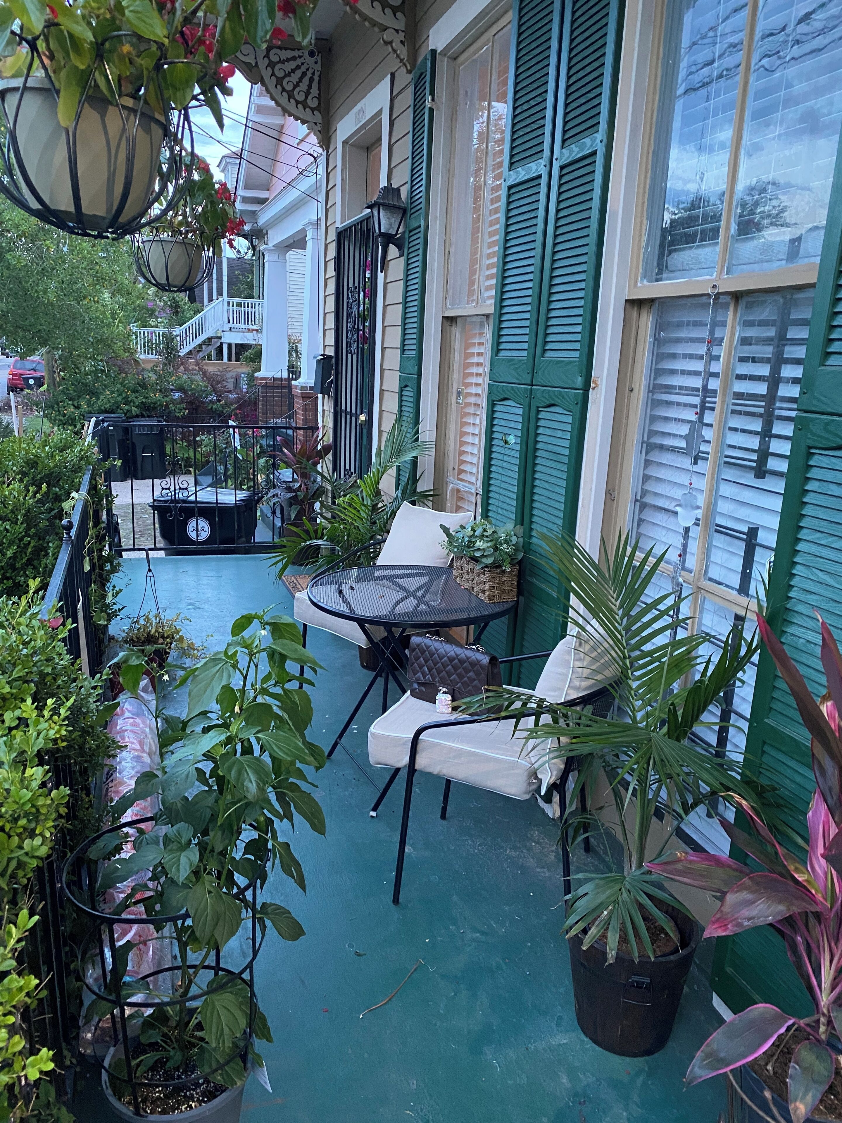 A covered patio with a table and chairs, surrounded by potted plants and a hanging light fixture.