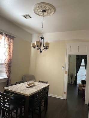 Uma sala de jantar com mesa de mármore, cadeiras de madeira escura, um candelabro e vista para outro ambiente.