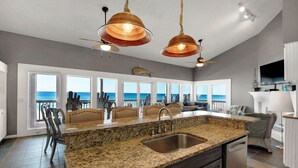 A spacious kitchen with granite countertops, a stainless steel sink, and pendant lighting. It features a large window overlooking the ocean, providing a view of the sea.