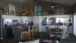 A spacious kitchen with white cabinets, a central island with chairs, a dining table, and a ceiling fan.