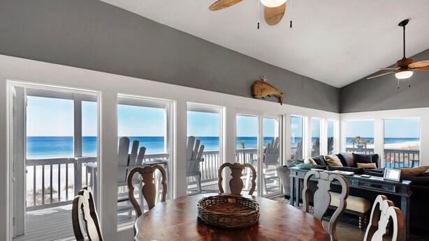 A dining area with a view of the ocean, featuring a wooden table, chairs, and a ceiling fan.