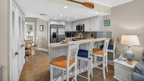 A modern kitchen with white cabinetry, a large island with bar stools, stainless steel appliances, and a wooden paddle on the ceiling. - Beautiful Modern Villa with OCEAN VIEWS! Screened Porch, Pool Access! (Isle of Palms)