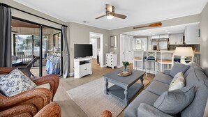 A spacious living area with a sofa, a coffee table, and a television. There is a sliding glass door leading to an outdoor patio. - Beautiful Modern Villa with OCEAN VIEWS! Screened Porch, Pool Access! (Isle of Palms)
