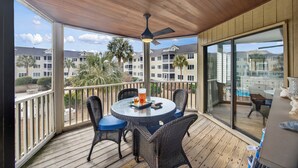 A covered outdoor area with a table and chairs, a ceiling fan, and a view of a residential area with palm trees and buildings. - Beautiful Modern Villa with OCEAN VIEWS! Screened Porch, Pool Access! (Isle of Palms)