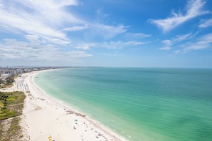 A beach with clear turquoise waters, a sandy shore, and a distant city skyline. - 5 star newly renovated condo 3 min. walk to the beach, bars, food & transport (St Pete Beach)