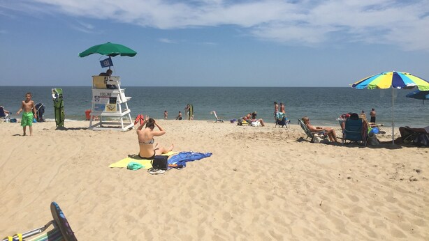 Ein Strand mit Rettungstürmen, Sonnenschirmen und entspannten Menschen.