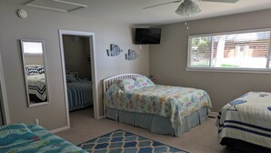 Ein Schlafzimmer mit zwei Betten, einem Deckenventilator, einem Fernseher und einem Fenster mit Jalousien.